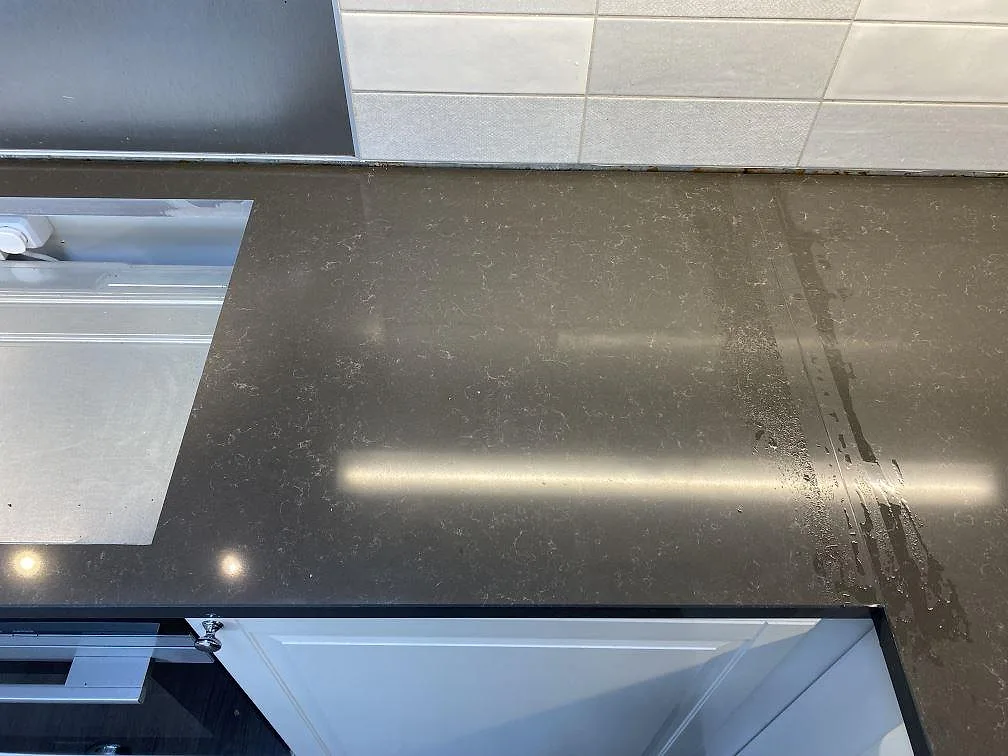Arbetsyta i polerad Technistone Noble Pietra Grey köksbänkskiva med diskho vid sidan och ljus kakelvägg i Kungsbacka.