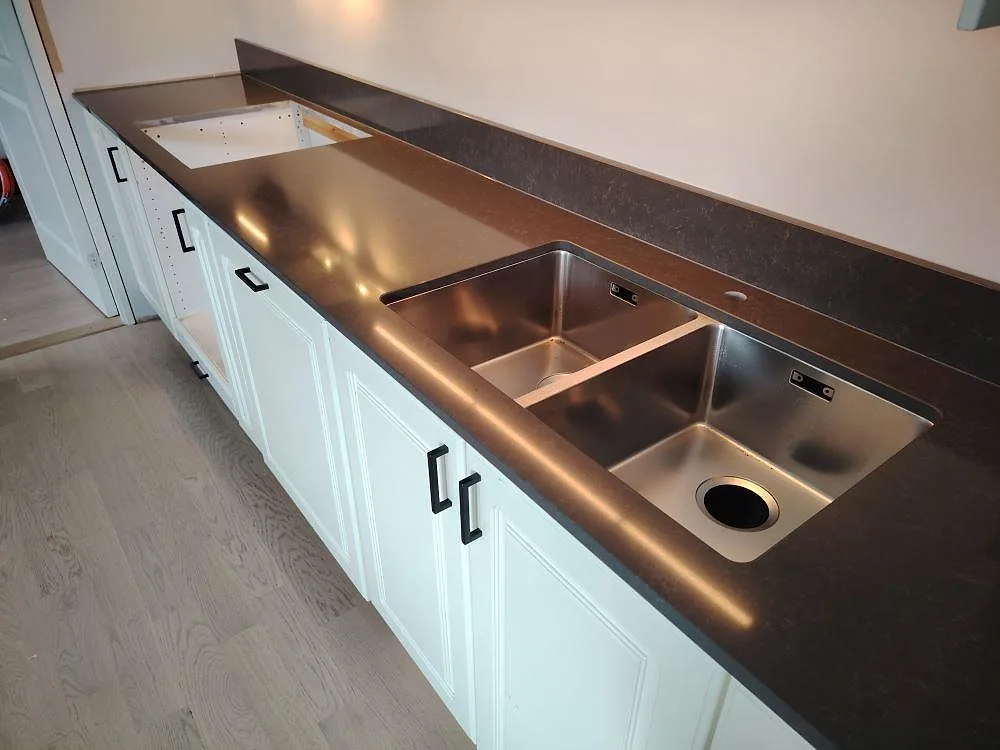 Närbild på polerad Technistone Noble Pietra Grey köksbänkskiva med rostfri diskho, rektangulärt urtag och matchande stänkkant i Vendelsö.