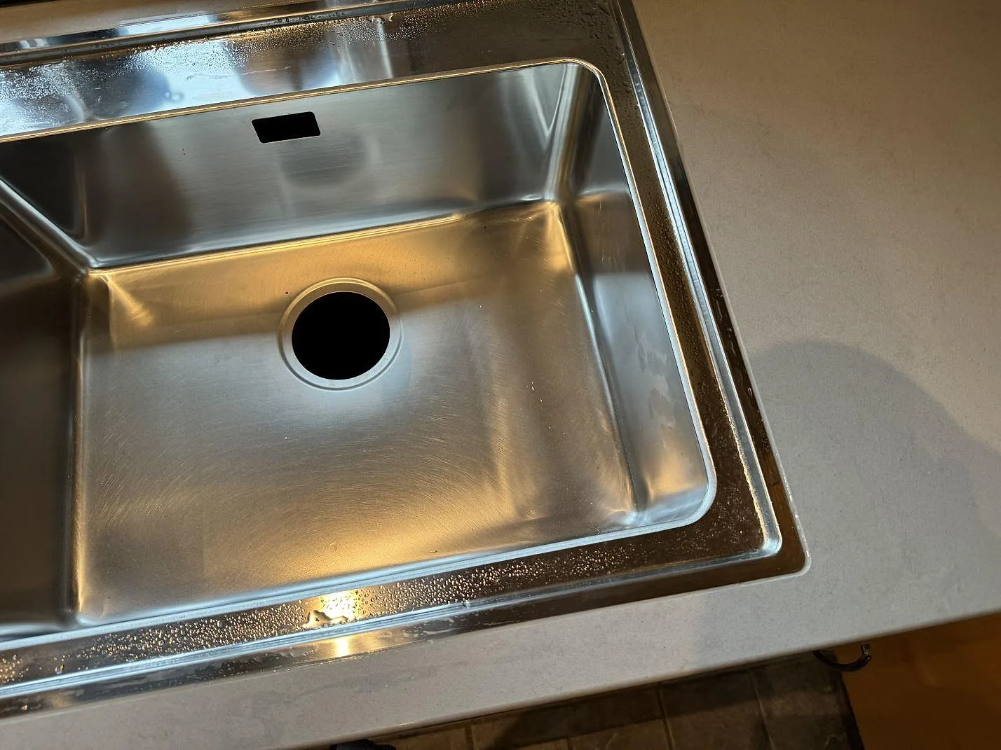 Detalj av rostfri diskho i en köksbänkskiva av polerad Technistone Noble Portland Grey komposit i Ellös.