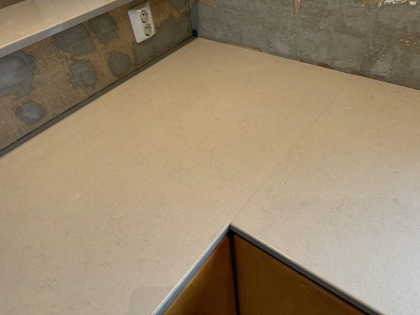 Detalj av hörn i köksbänkskiva i polerad Technistone Noble Portland Grey komposit intill ofärdig vägg i Ellös.