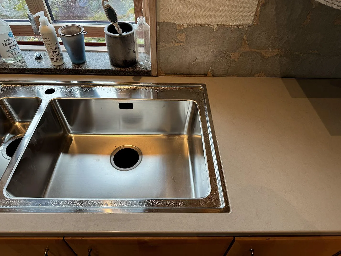 Köksbänkskiva i polerad Technistone Noble Portland Grey komposit med rostfri diskho vid fönster i Ellös.