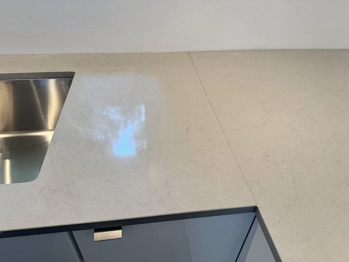 Detalj av L-formad köksbänkskiva i polerad Technistone Noble Portland Grey komposit intill rostfri diskho i Räng.