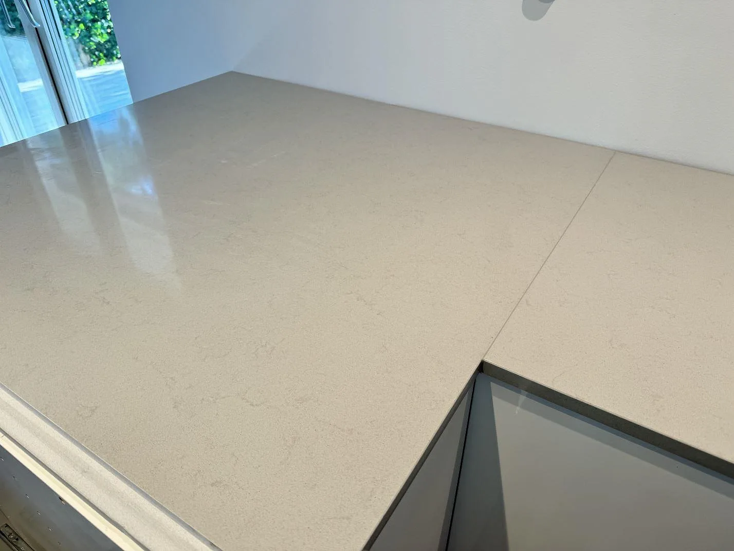 Närbild av polerad Technistone Noble Portland Grey komposit med ljusgrå struktur och fönsterreflektion i Räng.