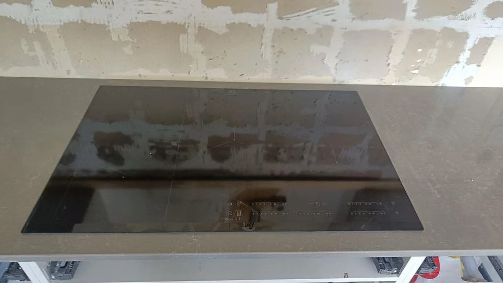 Detalj av svart induktionshäll infälld i polerad Technistone Noble Pro Cloud bänkskiva i ett kök i Västra Frölunda.