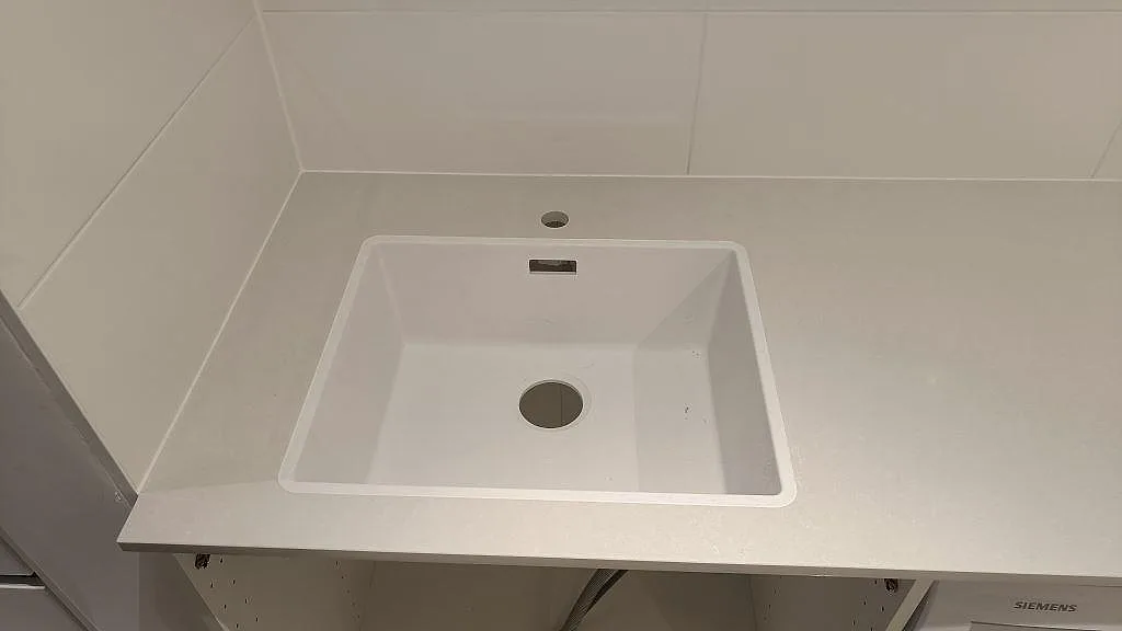 Närbild på den underlimmade vita kompositdiskhon i Technistone Noble Pro Frost med kranhål i stenen, polerad yta, i Jönköping.