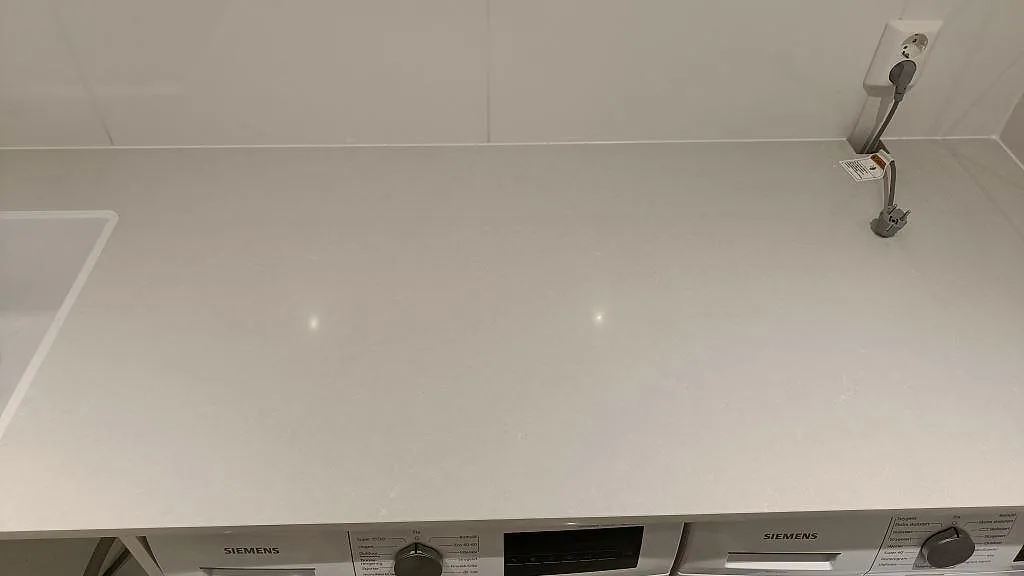 Bänkskiva i Technistone Noble Pro Frost ovanför två Siemens tvättmaskiner med eluttag indraget i stenytan, Jönköping.