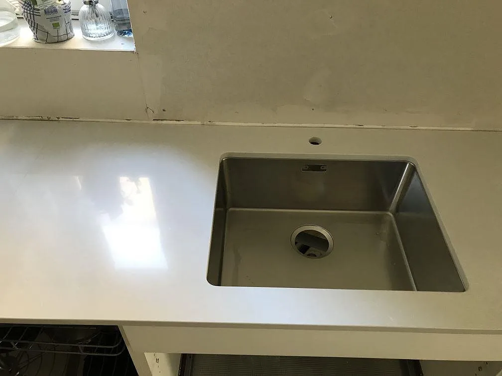 Underlimmad rostfri diskho med separat blandarhål i en polerad bänkskiva i Technistone Noble Pro Frost i ett kök i Limhamn.