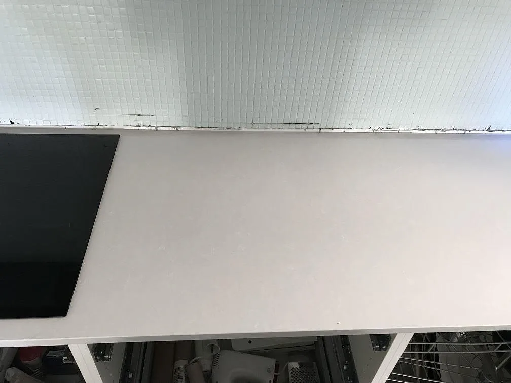 Polerad bänkskiva i vit Technistone Noble Pro Frost längs en köksvägg med infälld häll och vitt kakelstänkskydd i Limhamn.