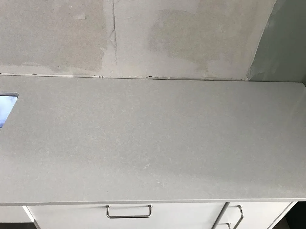 Ovanifrån av bänkskivan i vit Technistone Noble Pro Frost mot omålad vägg under monteringen i ett kök i Limhamn.