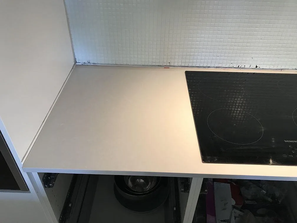 Hörnparti av köksbänkskivan i Technistone Noble Pro Frost med infälld häll och vitt mosaikkakel i ett kök i Limhamn.