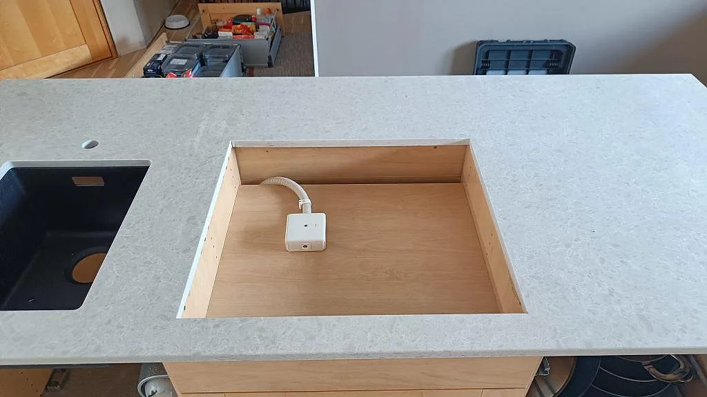 Köksbänkskiva i ljus Technistone Noble Quartzite, polerad, med öppning för häll i en halvö i Furulund.