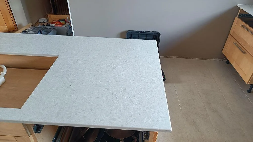 Ljus kvartskompositbänkskiva i Technistone Noble Quartzite på trästommar med framskjutande halvö i Furulund.
