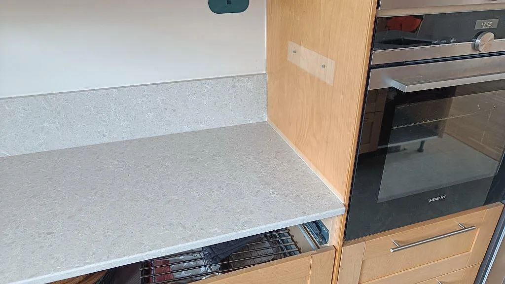 Polerad Technistone Noble Quartzite som köksbänkskiva och stänkkant vid ugn och träinredning i Furulund.