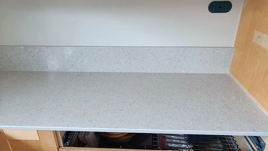 Rak köksbänk i Technistone Noble Quartzite med uppvikt stänkkant och ljusa trästommar i Furulund.