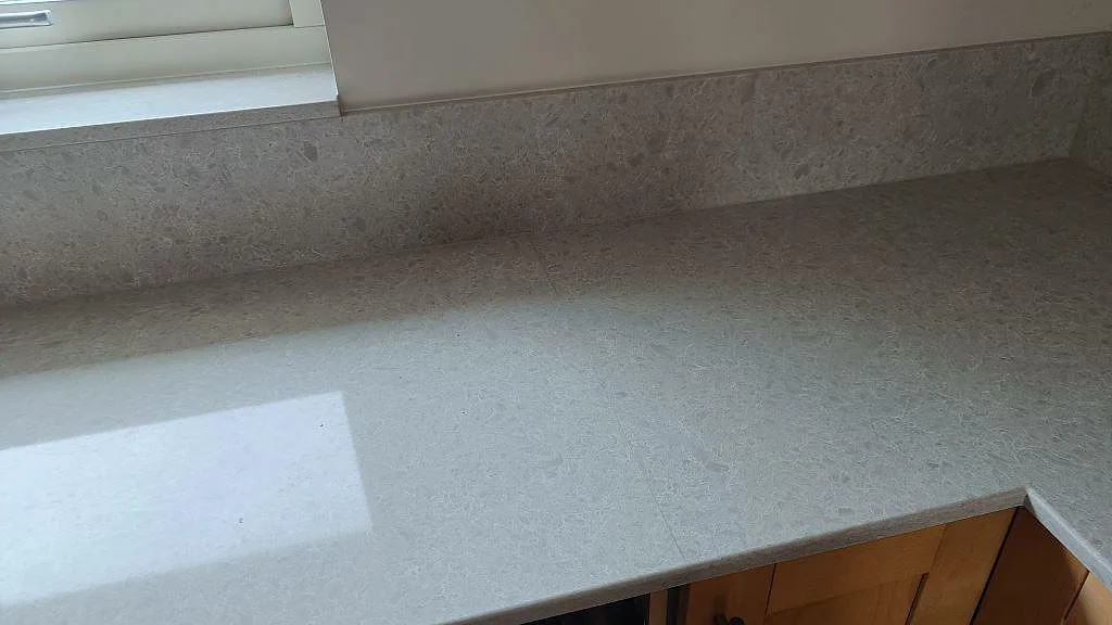 Ljus köksbänkskiva i Technistone Noble Quartzite med polerad yta, stänkkant och fönsterljus i Furulund.