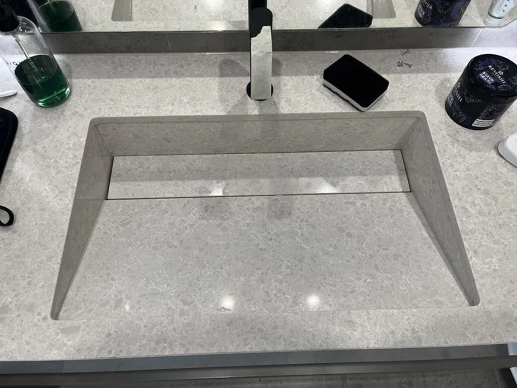 Närbild på polerad Technistone Noble Quartzite komposit runt en rektangulär tvättställsöppning och ett svart blandarhål i Huddinge.