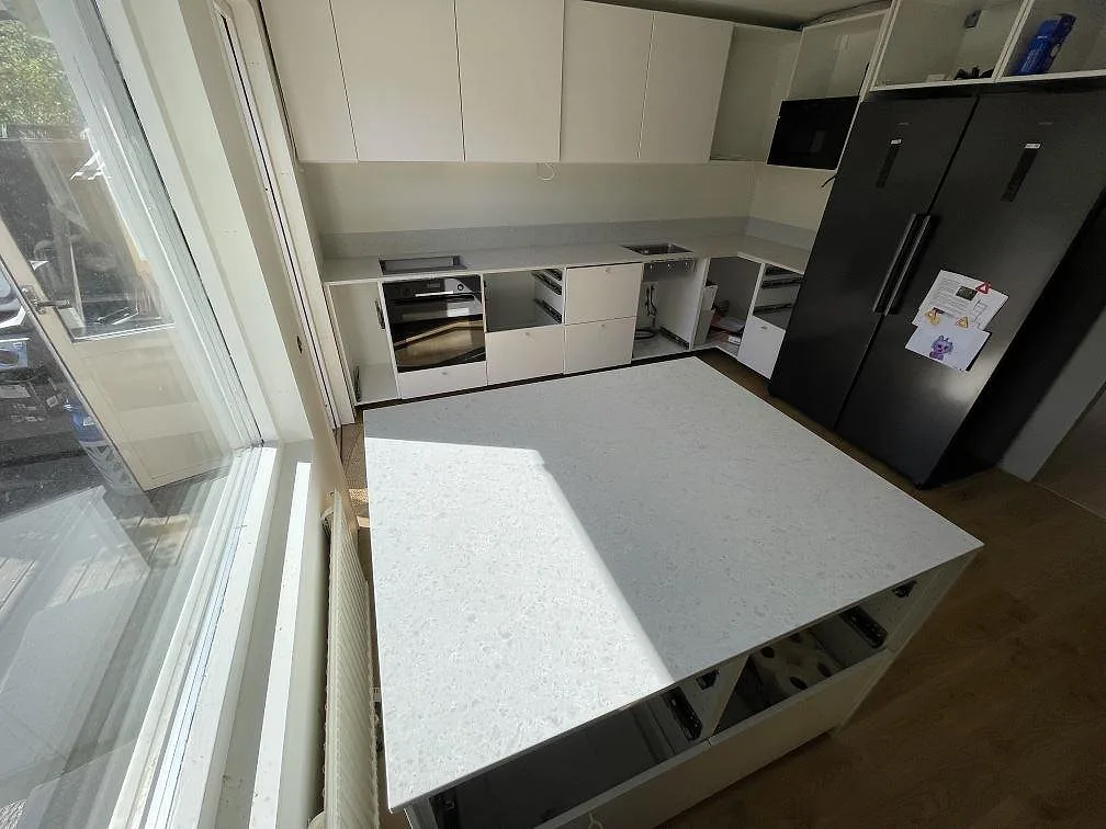 Toppvy över stor köksö i polerad Technistone Noble Quartzite med vitgrå komposityta och köksbänk bakom i Järfälla.
