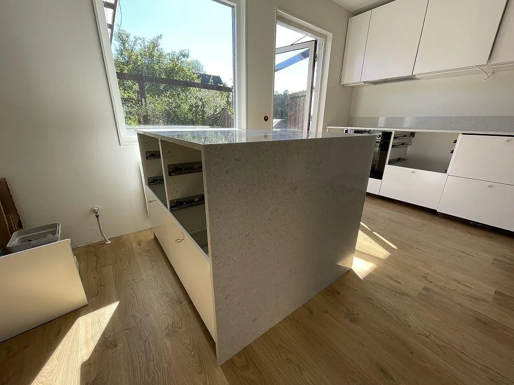 Köksö med neddragen sida i polerad Technistone Noble Quartzite, ljus kvartskomposit, fotograferad under montering i Järfälla.