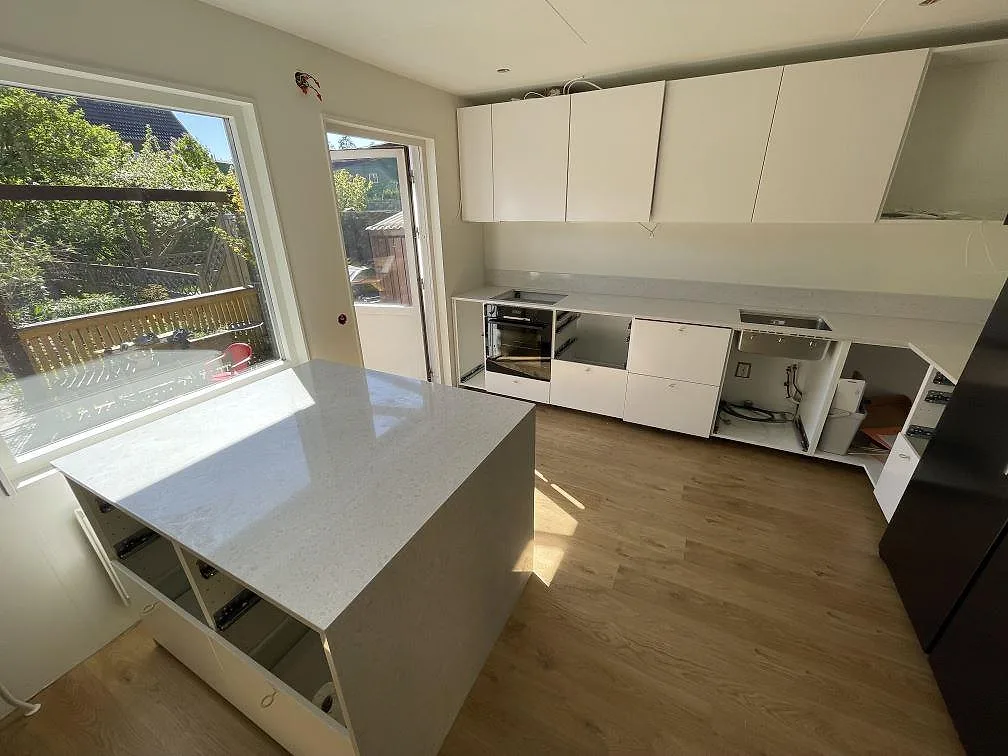 Köksbänkskiva i ljus Technistone Noble Quartzite, polerad kvartskomposit, med köksö och lång väggbänk i ett kök i Järfälla.