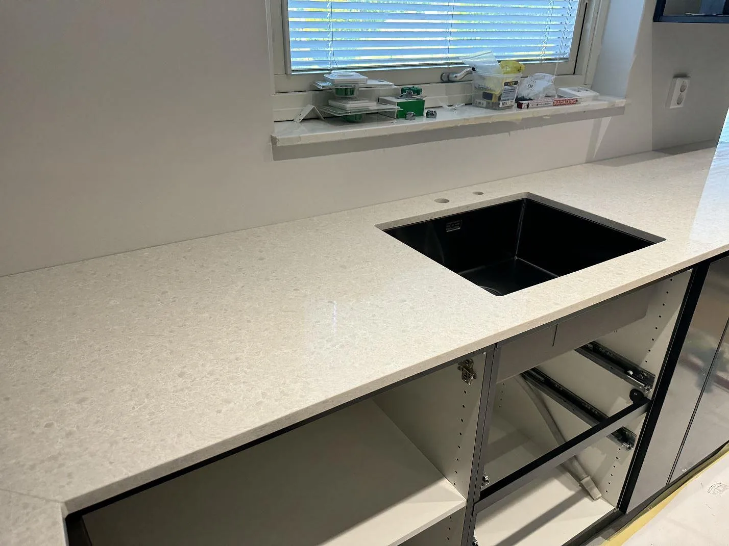 Köksbänkskiva i vit Technistone Noble Quartzite, polerad kvartskomposit, med svart underlimmad diskho under fönster i Malmö.