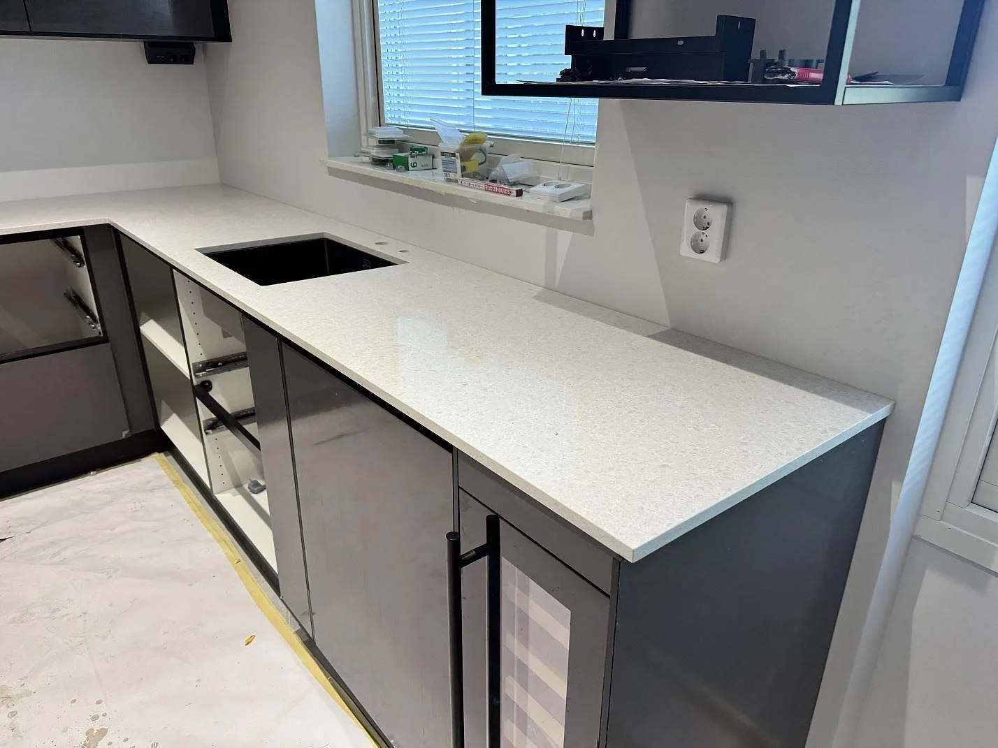 Lång köksbänkskiva i polerad Technistone Noble Quartzite i Malmö, med ljus kvartskomposit, fönster och mörkgrå fronter under montering.