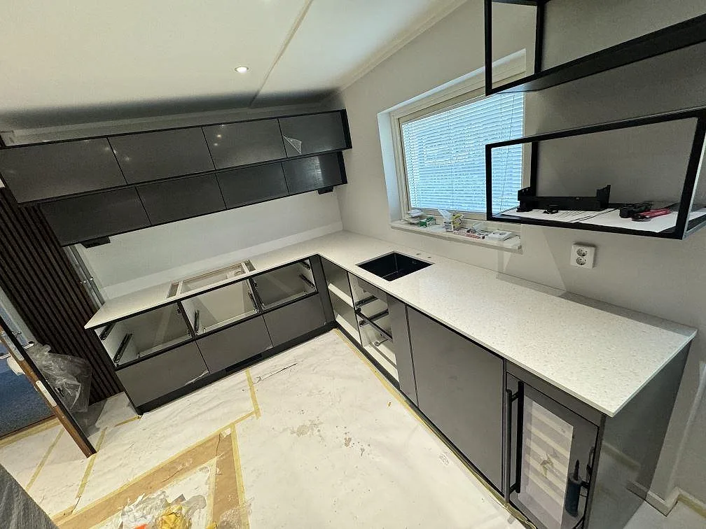 L-format kök i Malmö med 20 mm polerad Technistone Noble Quartzite i ljus kvartskomposit, svart underlimmad diskho och grå köksstommar.