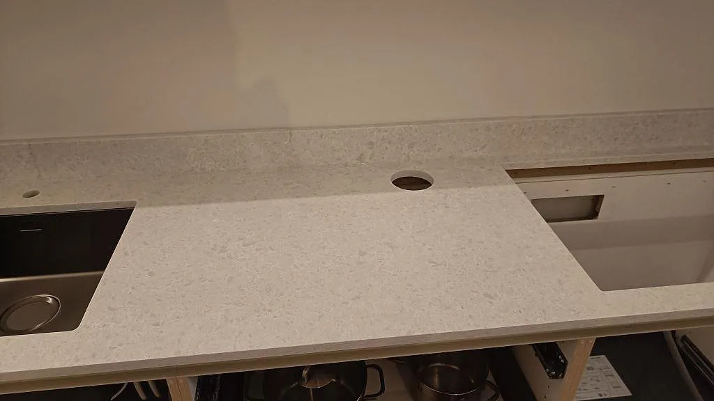 Bänkskiva i Technistone Noble Quartzite med diskho, rund blandaröppning och rektangulärt urtag under montering i Malmö.