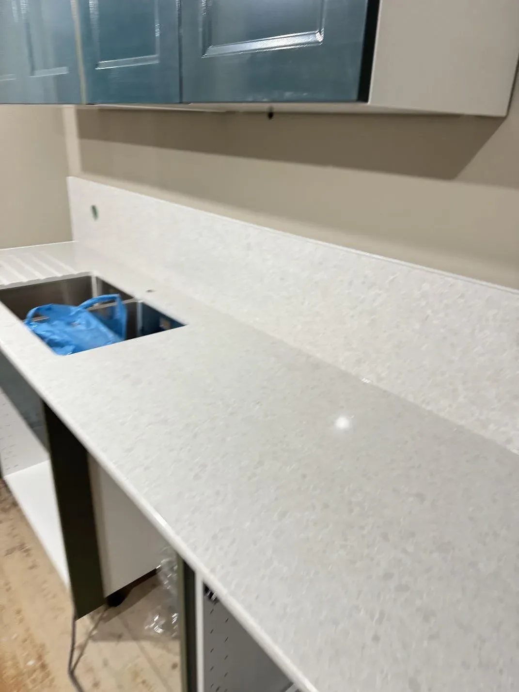 Lång köksbänkskiva i polerad Technistone Noble Quartzite med låg stänkkant och öppet diskhohål under montering i Staffanstorp.