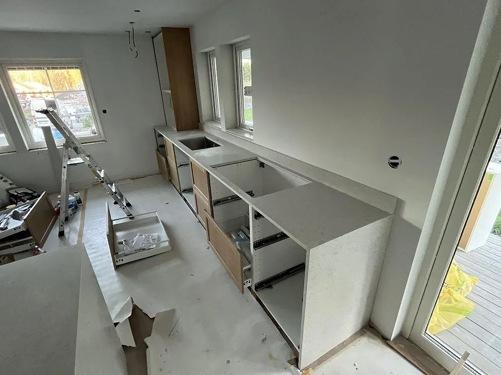 Väggbänk i matt Technistone Noble Quartzite med låg kant mot väggen och öppna köksstommar under montering i Upplands Väsby.