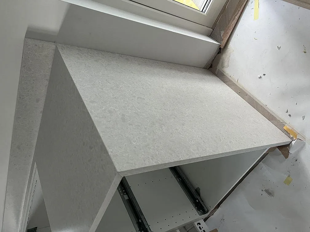 Detalj av matt Technistone Noble Quartzite som sidobänk vid fönster, med ljus ådring och öppen köksstomme i Upplands Väsby.