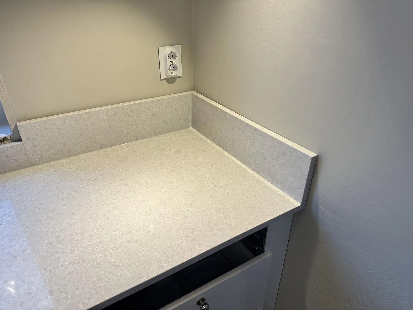 Hörnvy av polerad Technistone Noble Quartzite bänkskiva i komposit med uppvikt stänkkant och vägguttag i Västra Frölunda.