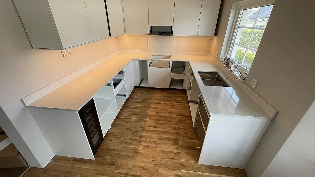U-formad köksbänkskiva i ljus Technistone Noble Quartzite, polerad, med stänkkant i ett kök i Vellinge.