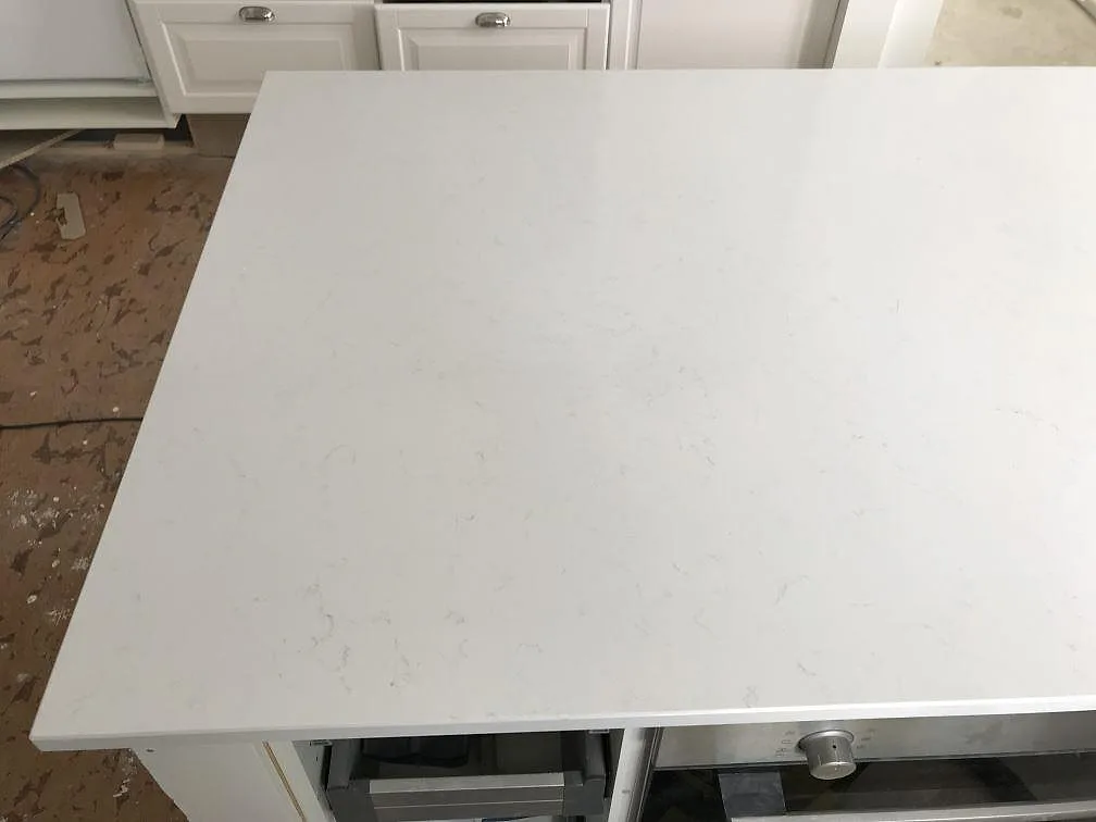 Köksö med bänkskiva i vit Technistone Noble Supreme White, polerad yta med diskret ådring, i ett kök under montering i Bjärred.