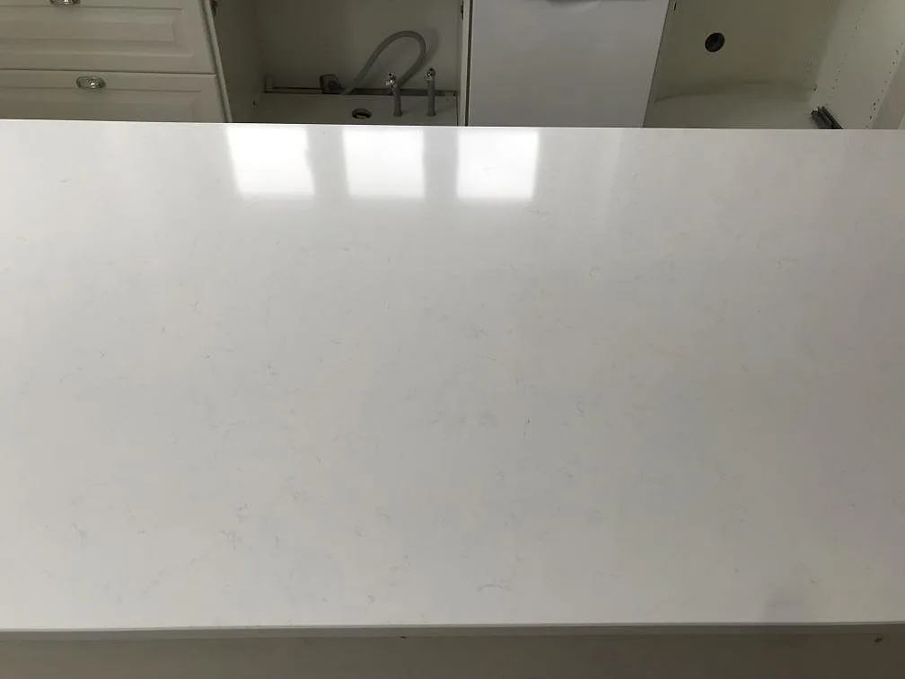 Blank polerad bänkskiva i vit Technistone Noble Supreme White med spegling i ytan och köksblandare i bakgrunden i ett kök i Bjärred.