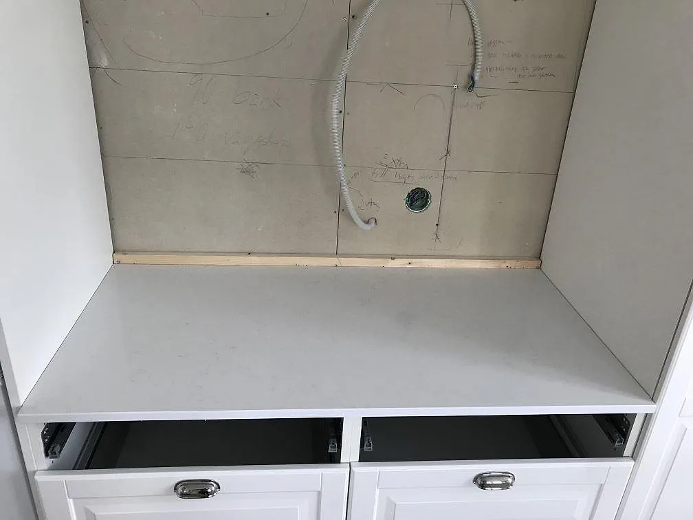 Installerad bänkskiva i vit Technistone Noble Supreme White mot oputsad vägg med lådfronter under, i ett kök i Bjärred.