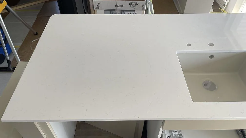 Detalj av den polerade vita kvartskompositskivan Technistone Noble Supreme White vid diskhon, med mjuk grå ådring i Falköping.