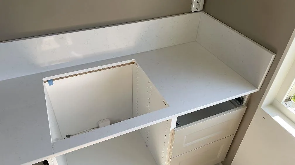 Hörnvy av polerad Technistone Noble Supreme White köksbänkskiva med låg stänkkant och plats för häll i Falköping.