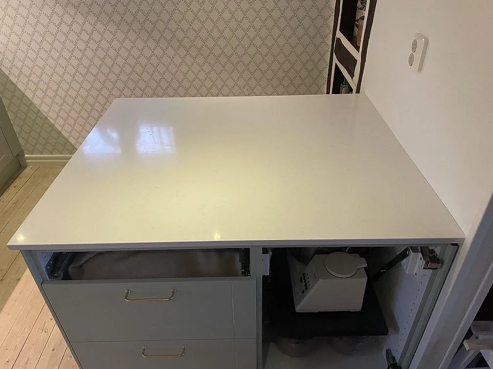 Köksö med blank bänkskiva i Technistone Noble Supreme White, polerad kvartskomposit, i ett kök i Fjälkinge med öppna stommar.