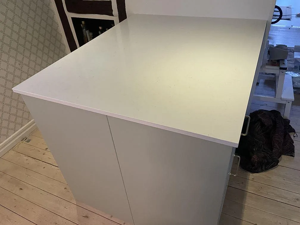 Närbild på köksö i vit Technistone Noble Supreme White, polerad komposit, med rak kant och monteringsdetaljer i Fjälkinge.