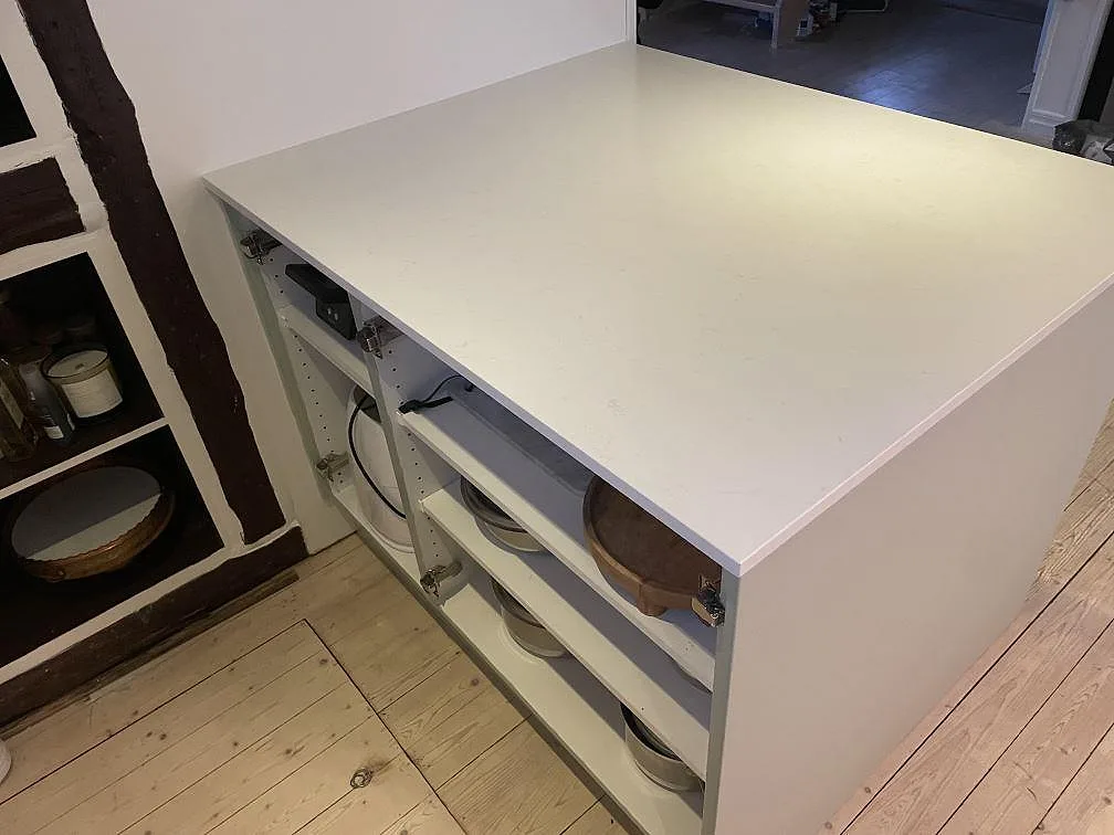 Köksö sedd från sidan med bänkskiva i polerad Technistone Noble Supreme White, vit kvartskomposit, och öppna hyllor i Fjälkinge.