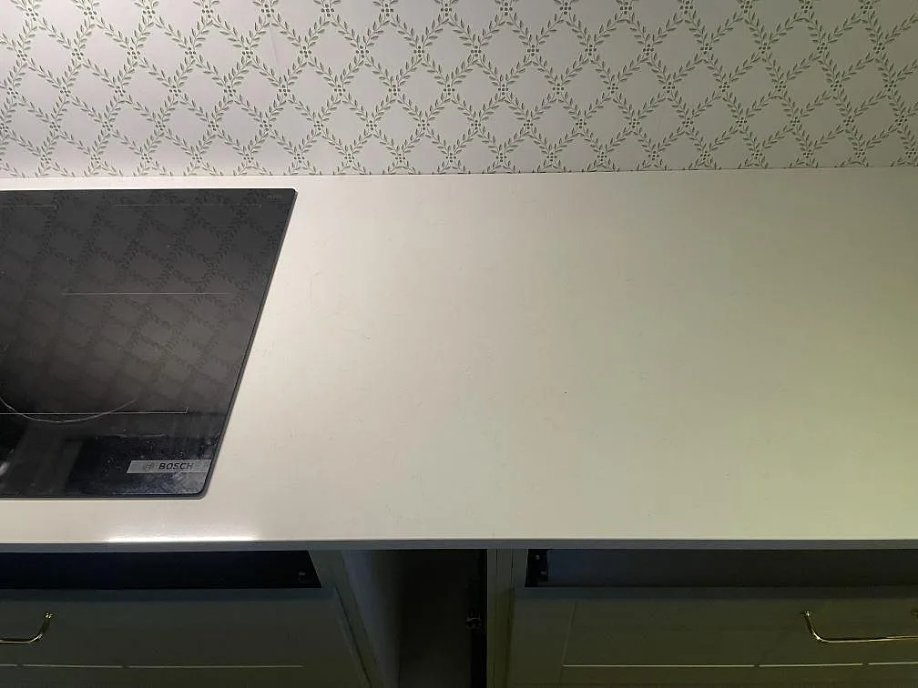Detalj av väggbänk i polerad Technistone Noble Supreme White, vit komposit, med häll och mönstrad vägg i kök i Fjälkinge.
