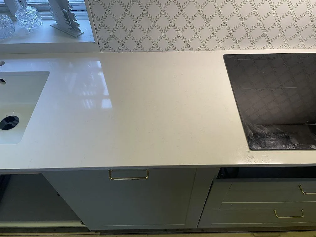 Väggbänk i polerad Technistone Noble Supreme White, vit komposit, med diskho och häll i ett kök i Fjälkinge.