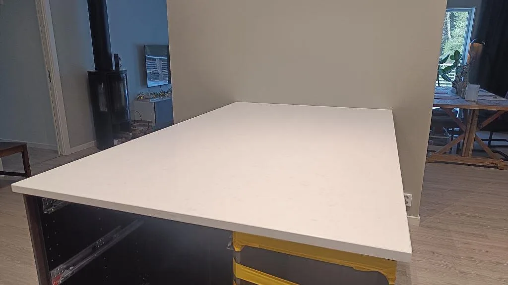 Stor rektangulär köksbänkskiva i polerad Technistone Noble Supreme White med rak kant i ett kök under montering i Floda.