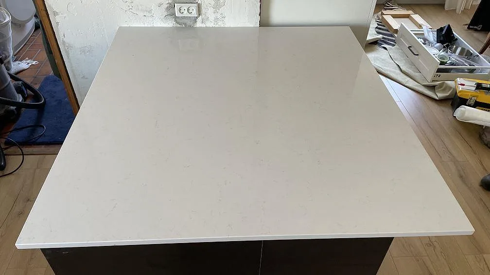 Köksö i polerad vit Technistone Noble Supreme White med diskret ådring i ett kök under montering i Greve.