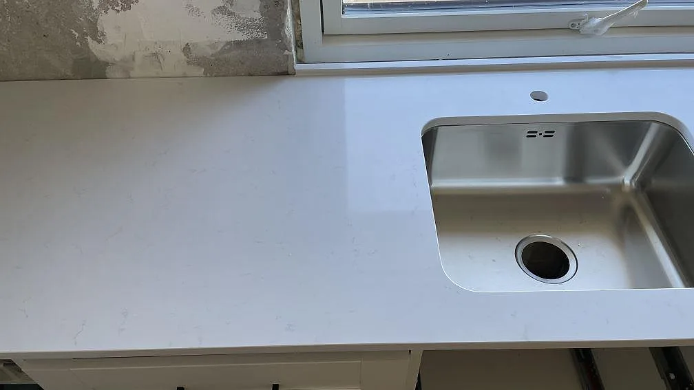 Underlimmad rostfri diskho i polerad vit Technistone Noble Supreme White köksbänkskiva under ett fönster i Greve.