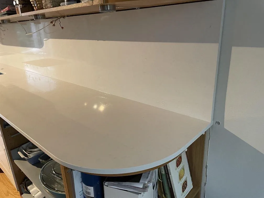 Lång arbetsyta i vit Technistone Noble Supreme White komposit, polerad, med matchande stänkskydd under överskåp i Hässleholm.
