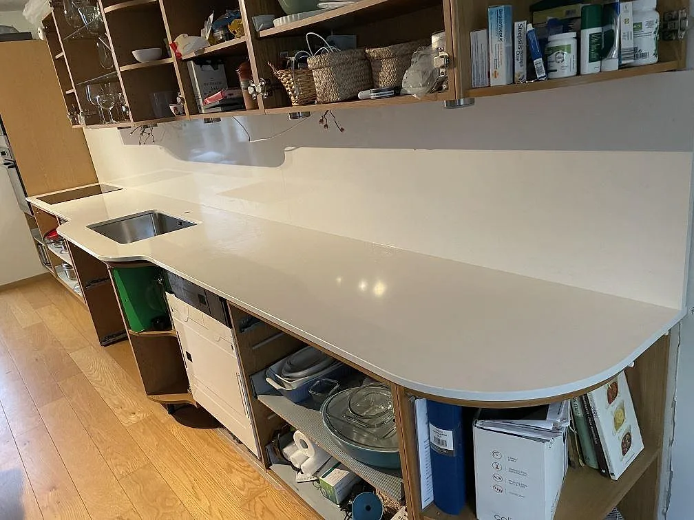L-formad köksbänkskiva i vit Technistone Noble Supreme White komposit, polerad, med rostfri diskho och svart induktionshäll i Hässleholm.