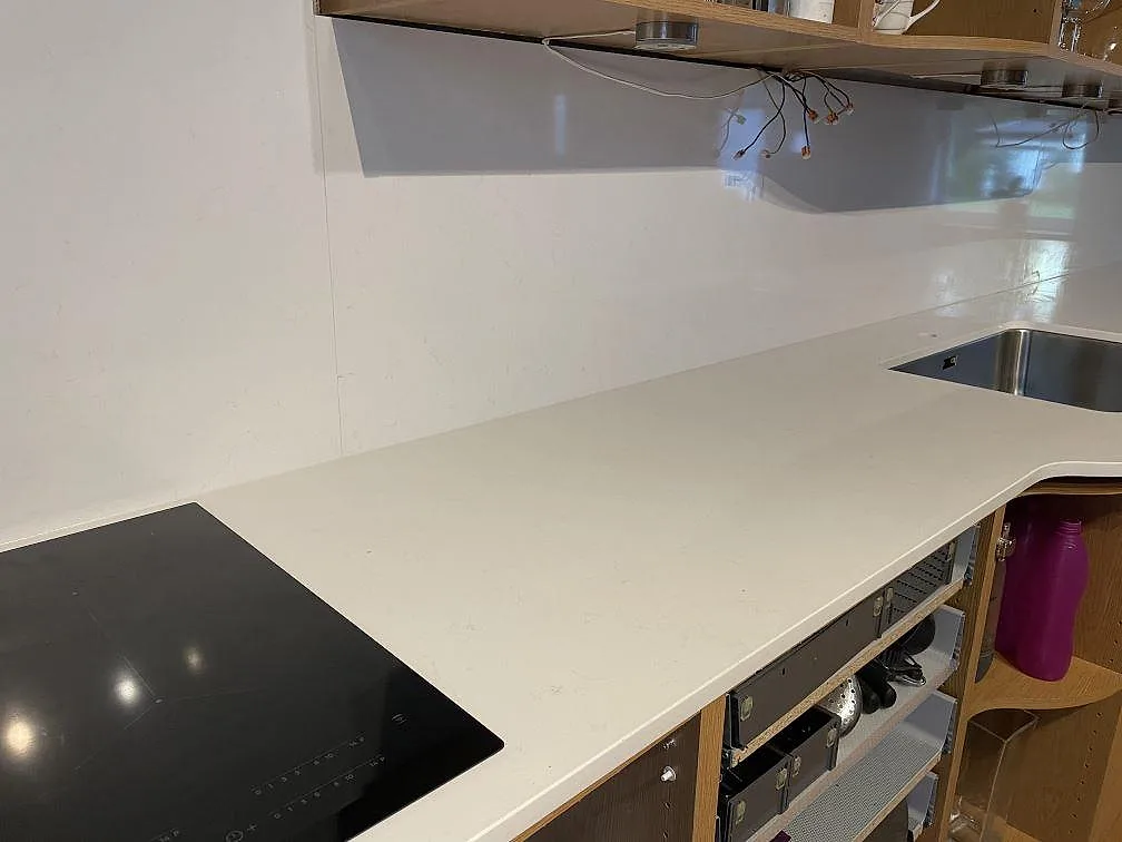 Polerad köksbänkskiva i Technistone Noble Supreme White med svart induktionshäll, underlimmad rostfri diskho och stänkskydd i Hässleholm.