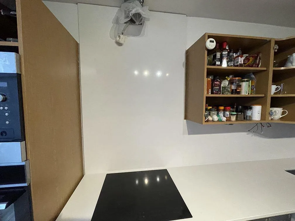 Hällsidan av köket med polerad Technistone Noble Supreme White komposit, svart induktionshäll och stänkskydd i Hässleholm.