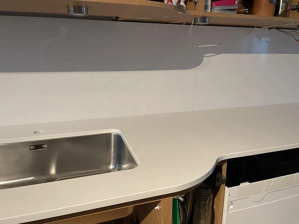 Köksbänk i polerad Technistone Noble Supreme White komposit med rostfri diskho, rundad framkant och öppna stommar i Hässleholm.